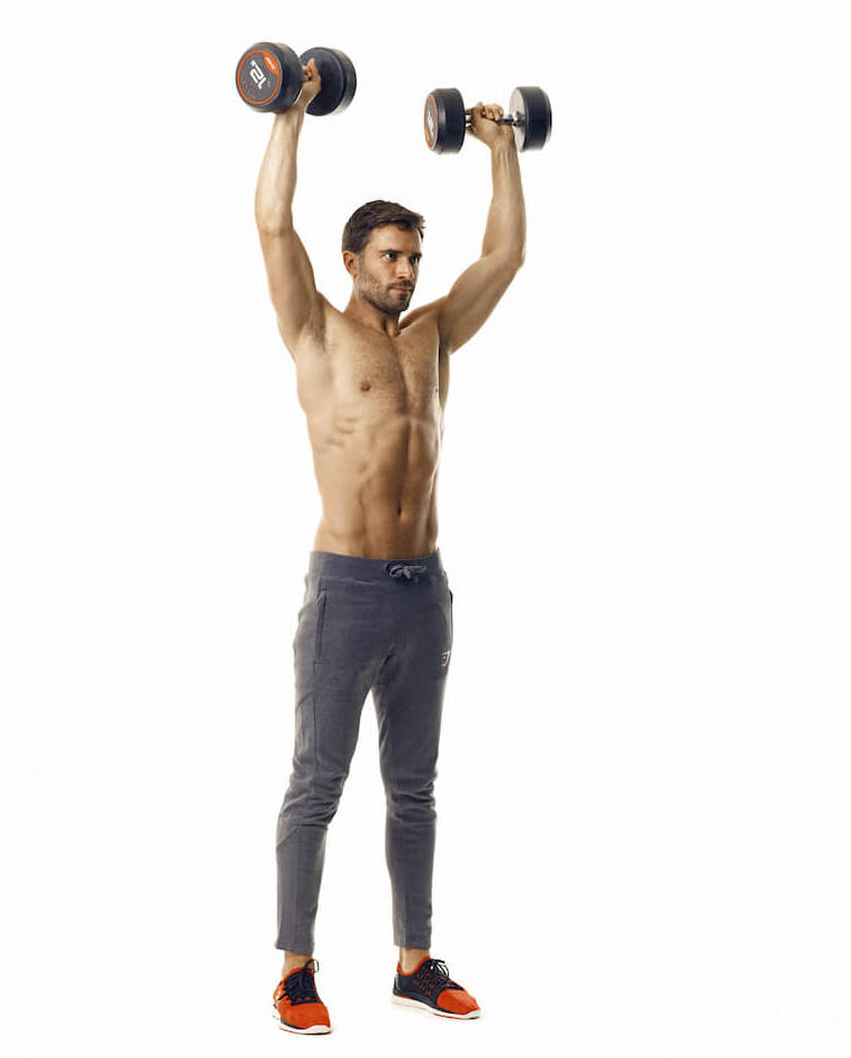 man demonstrates step two of dumbbell overhead press; he stands tall with a dumbbell in each hand, pushing them upwards above his head