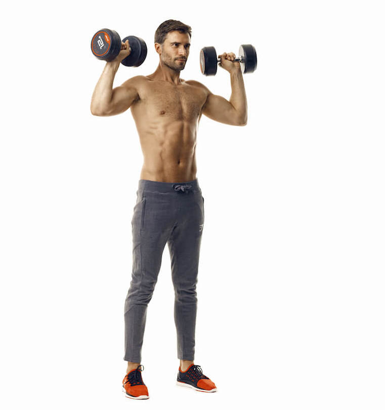 man demonstrates step one of dumbbell overhead press; he stands tall with a dumbbell in each hand, held at shoulder height with bent arms