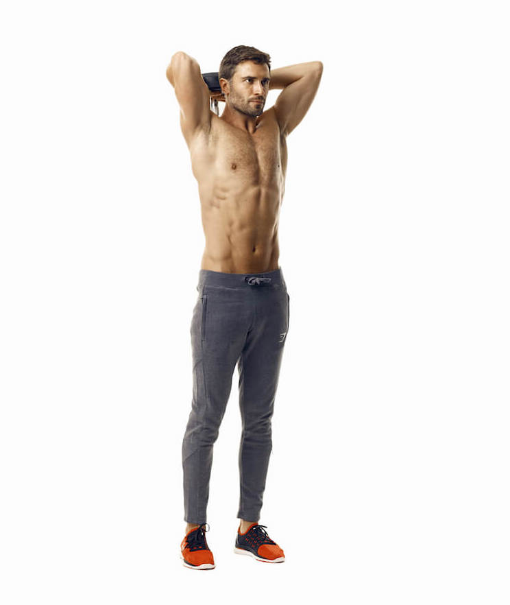 man demonstrates step one of dumbbell triceps extension; standing upright, he holds a dumbbell behind his head using both hands