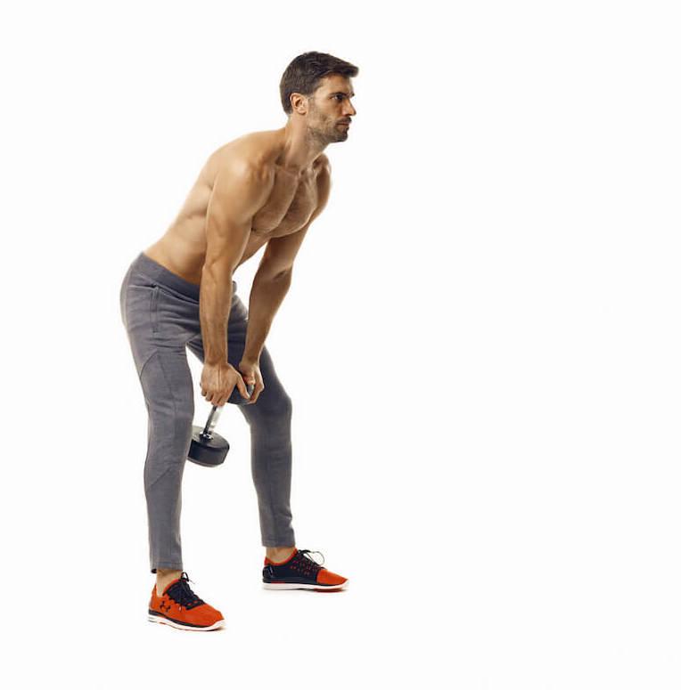 man demonstrates step one of dumbbell swing; standing upright, he bends forwards at the hips as both hands hold a dumbbell between his legs in home dumbbell hiit workout
