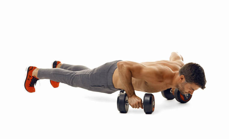 man demonstrates step one of dumbbell press up renegade row; in a plank position, with each hand balanced on a dumbbell, he bends his arms to lower himself into a press up position