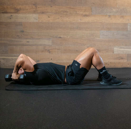 man demonstrated rolling extension; laying on floor with knees bent, he rolls weights behind his head