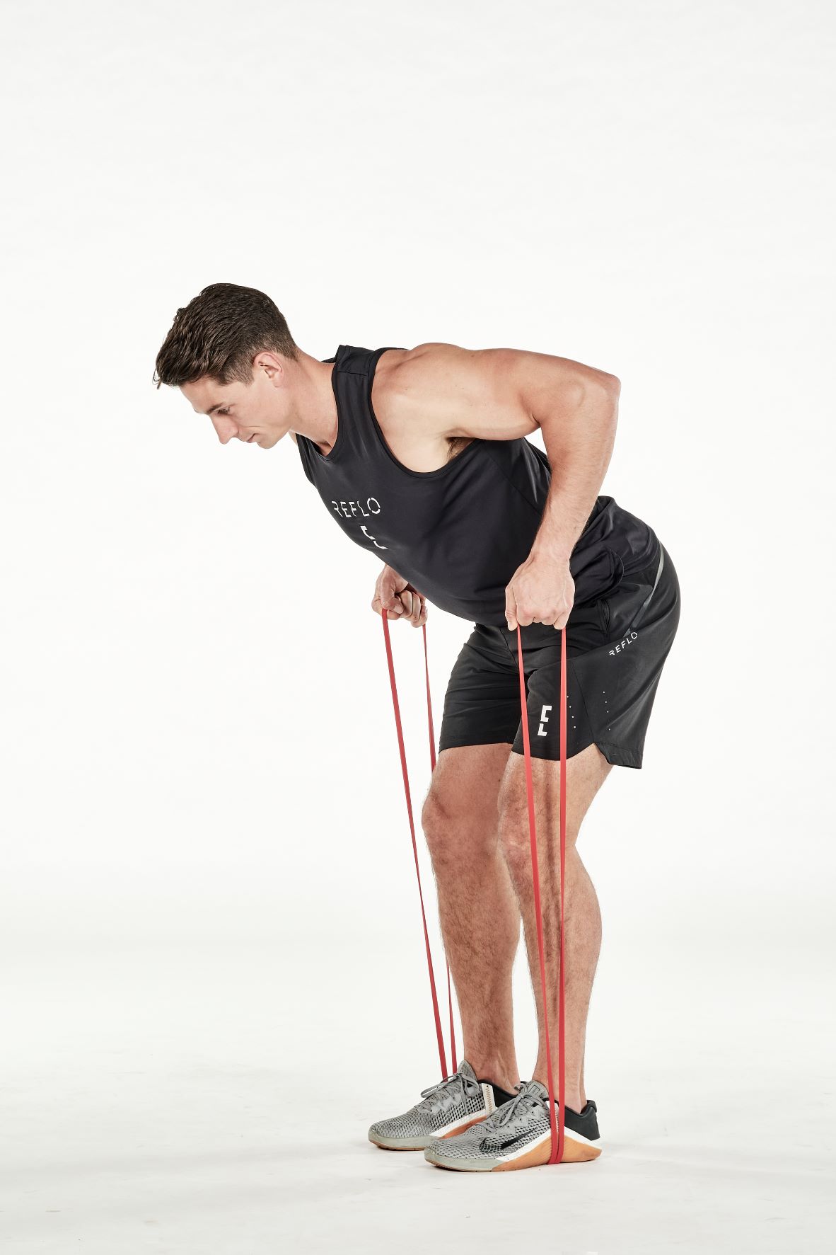 man demonstrating step two of resistance band bent over row; he is bent over at the hips, knees slightly bent, pulling up on a band that is wrapped around his feet; he wears a black fitness vest, black shorts and trainers