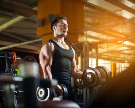 A man in a balck vest lifting dumbbells in a gym - how to get bigger arm muscles