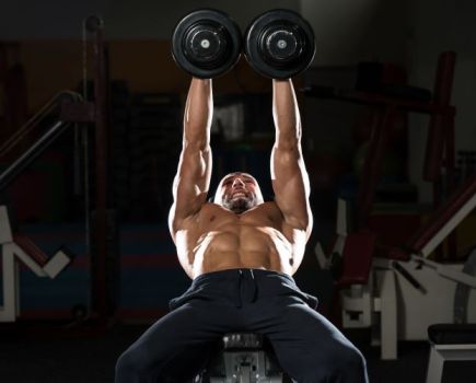 Man on a gym bench performing a dumbbell bench press