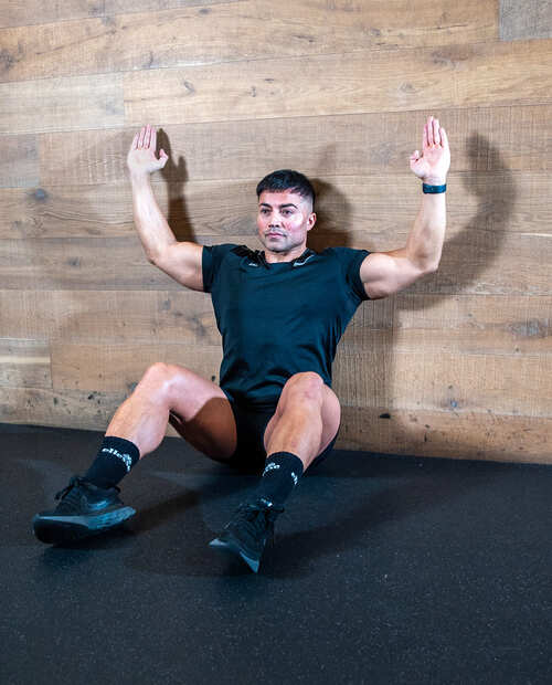 Part of the best full-body dumbbell workout: a man demonstrating floor sliders, sitting with arms raised