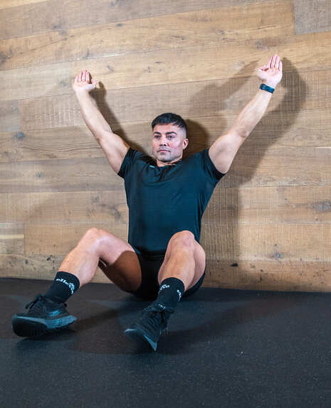 Part of the best full-body dumbbell workout: a man demonstrating floor sliders; seated against a wall, he slides his hands up and down behind him