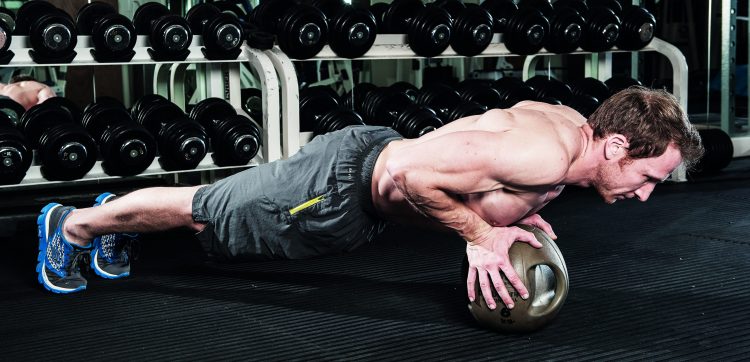 Man perfoming end of medicine ball press-up in gym - how to grow bigger arm muscles