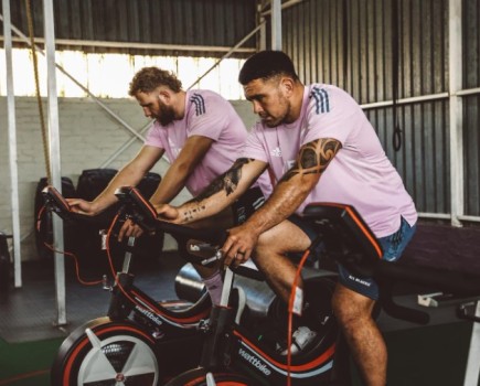 Two All Black rugby players exercising on stationary bikes