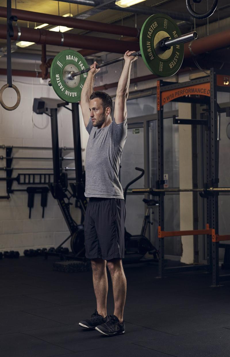man demonstrating overhead press in full body gym workout session