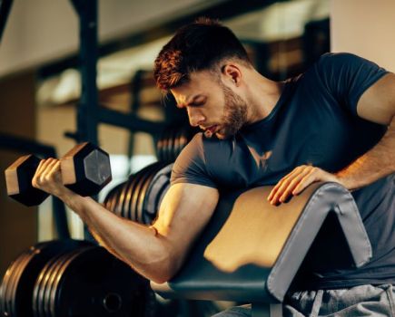Man in gym performing preacher curl on incline bench