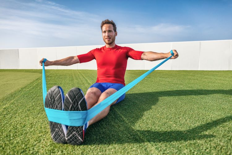 A man sitting on grass performing resistance band exercises