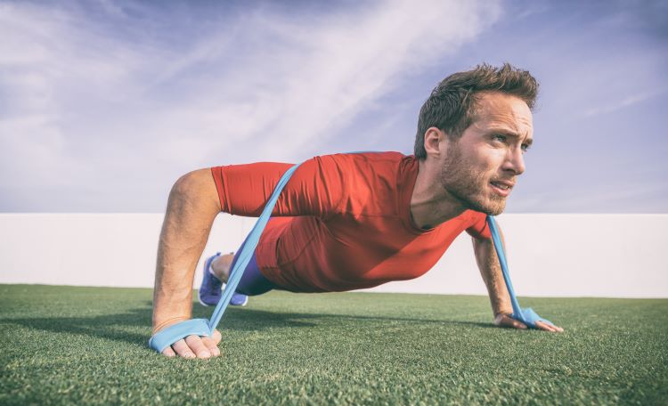 Man outdoors in red shirt doing pushups with a resistance band