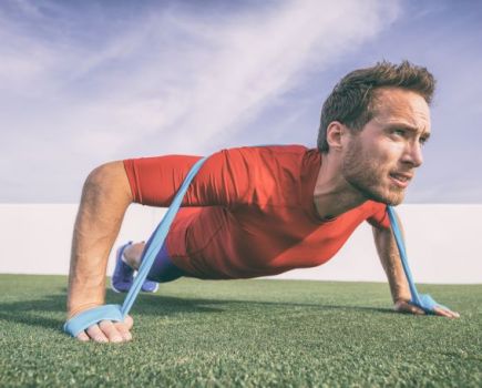 Man outdoors in red shirt doing pushups with a resistance band