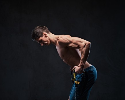 topless man performing resistance band row against black background