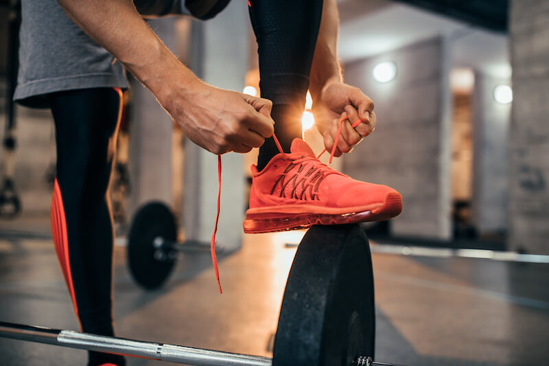 Cropped image of man with foot elevated tying the laces of an orange gym shoe