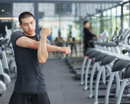 man performing shoulder stretches in the gym