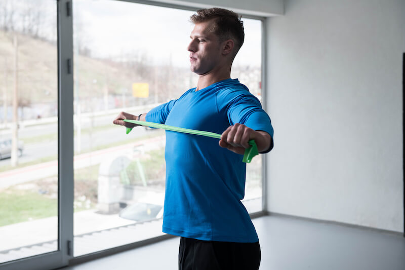 Man in blue long sleeve top using a resistance band for a warm-up exercise