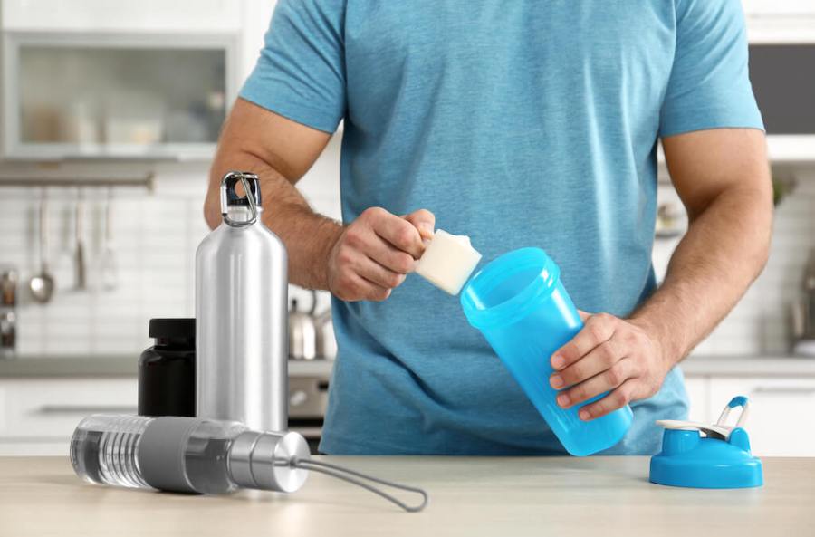 Man in blue t-shirt putting protein powder into shaker bottle