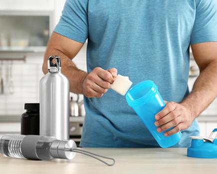 Man in blue t-shirt putting protein powder into shaker bottle