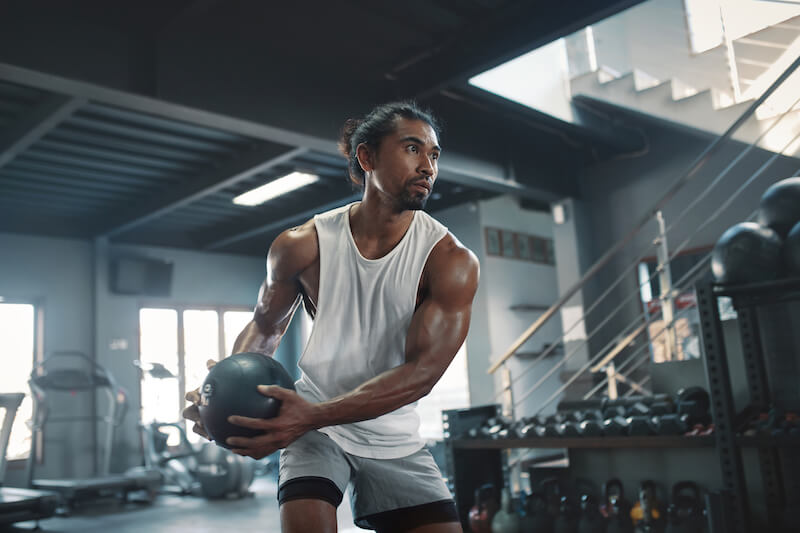 man in gym performing exercise with medicine ball