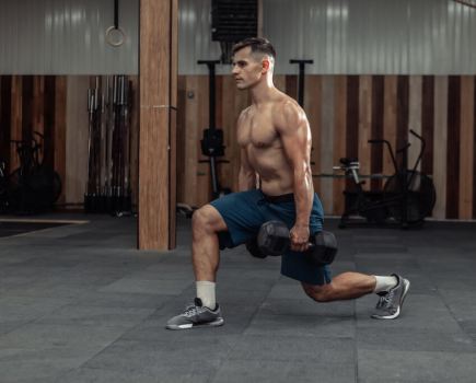 topless man performing dumbbell lunge in gym