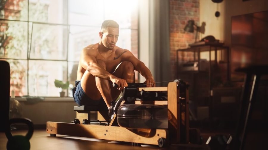 Topless man using rowing machine in home gym