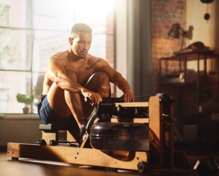 Topless man using rowing machine in home gym