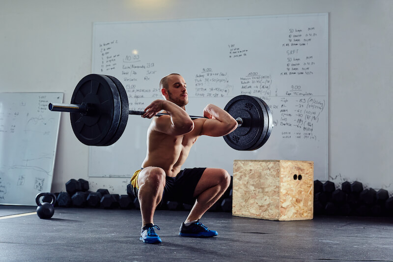 man in gym performing front squat with barbell