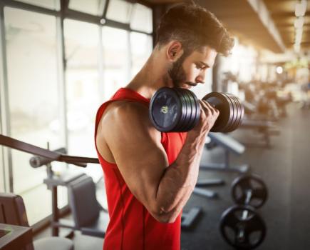 man working out with dumbbells in gym, wearing red top