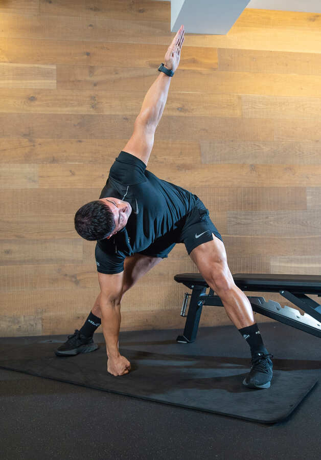 Part of the best full-body dumbbell workout: a man demonstrates t-spine rotations, twisting to the left with arms outstretched