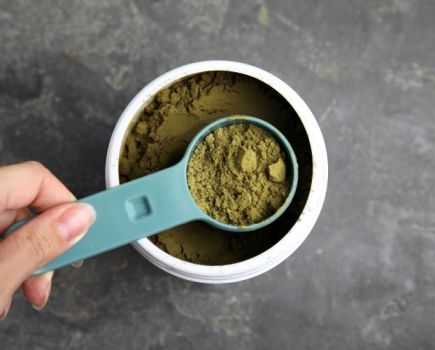 A scoop and tub of green vegan protein powder