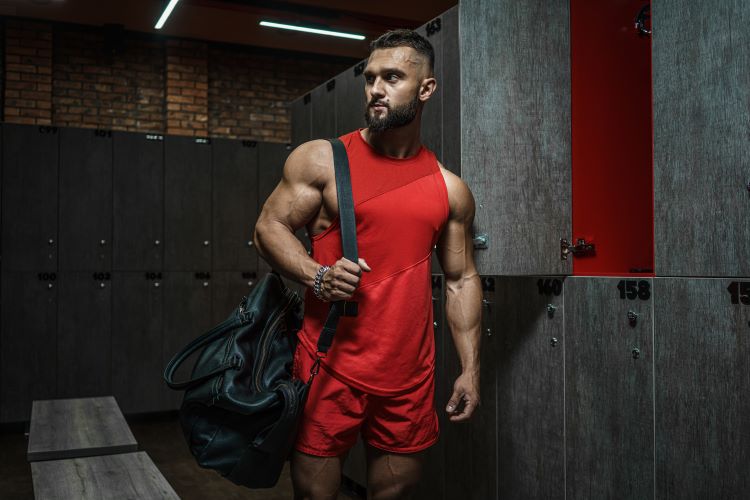 A man wearing red gym kit with a gym bag in a locker room