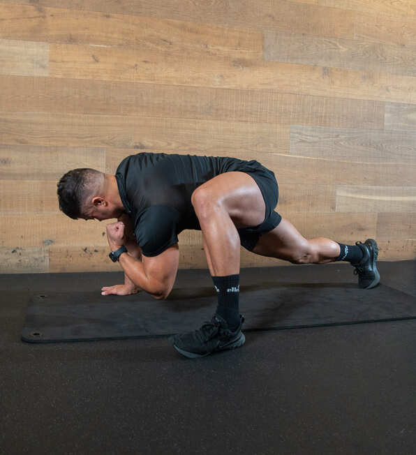 Part of the best full-body dumbbell workout: world's greatest stretch demonstration part 3; one leg behind him, one to the side, he curls his arm under his body to stretch his back